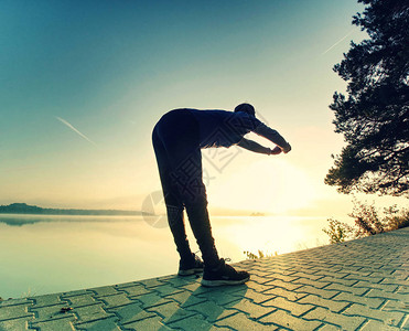 短暂的喘息日出时在湖滩上锻炼和伸展的活跃男子的剪影健图片