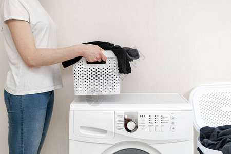 白色洗衣篮的裁剪照片与女人手中的衣服站在洗衣机附近明亮图片