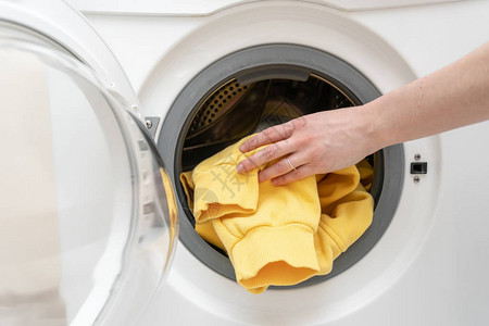 妇女用手把衣服装在白色现代洗衣机上的照片被剪裁和关闭图片