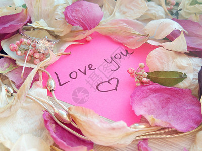 爱您在粉红粘贴纸条上的留言上面有干玫瑰兰花瓣银首饰戒指和木图片