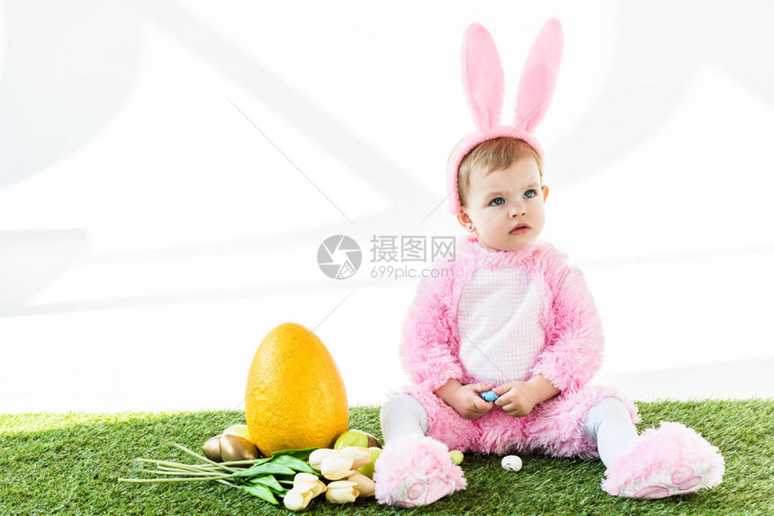 穿着有趣的装扮的可爱婴儿坐在多彩鸡蛋郁金香和黄蛋旁图片