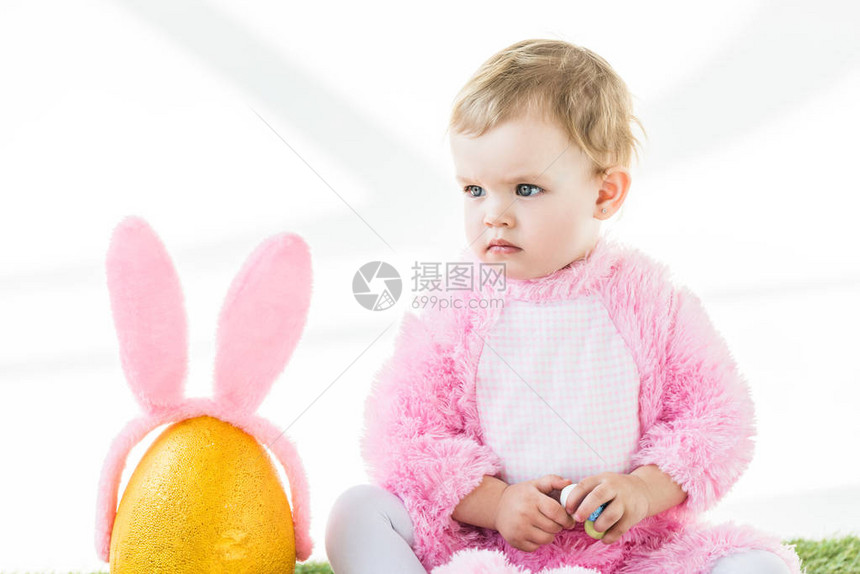 穿着粉红长毛花装的可爱孩子拿着多彩的蛋坐在黄乌龟鸡蛋附近白边被图片