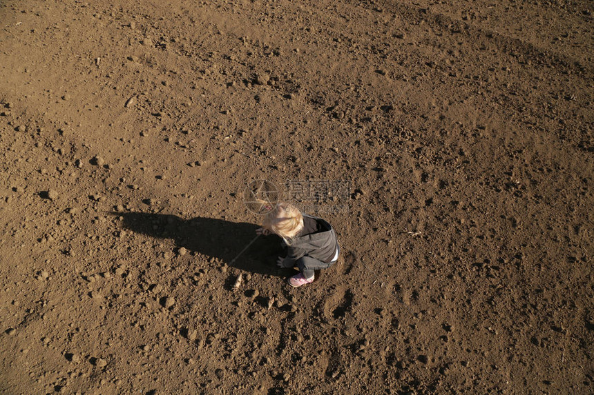 在平坦的农田上玩泥土的可爱女婴图片