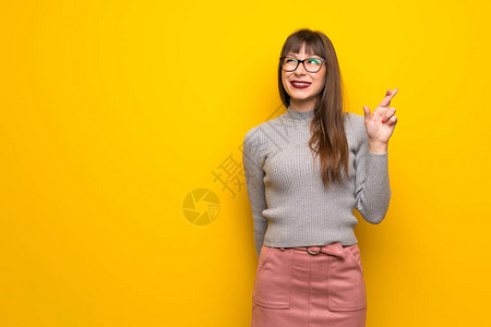 女人在黄色的墙上戴眼镜手指交叉并图片