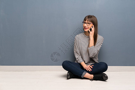 坐在地板上戴眼镜的妇女与移动电话保持对话图片