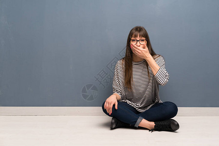 戴眼镜坐在地板上双手用盖住嘴的女人图片