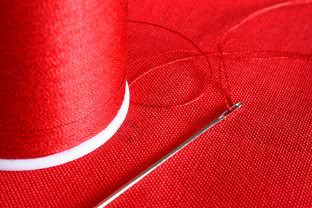 红色织物上的红色线轴和缝纫针的特写图像图片
