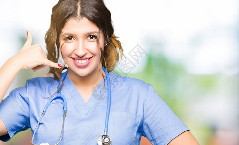 身穿医疗制服的年轻女医生微笑着用手和指做电话手势图片