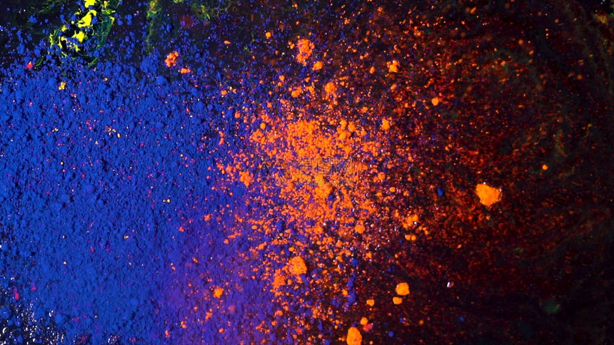 光亮的彩色粉末跌落和混合的顶端景象干橙色和蓝墨水落在黑色背景图片