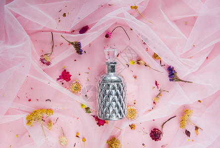 香水瓶和粉红色薄纱上的干花自然光图片