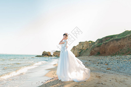 美丽的新娘穿着豪华婚纱与海边的花束穿着蓝色连衣裙的新娘沿着海边散步图片