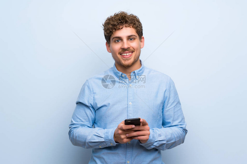 蓝墙上的金发男子用手机发送消息图片