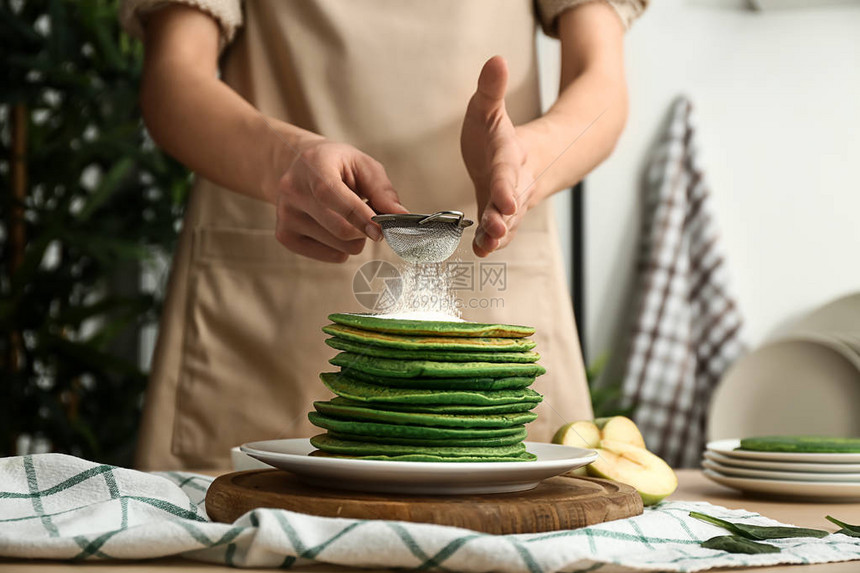 女人在厨房里将糖粉洒在美味的绿色煎饼上图片