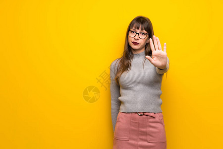 在黄色墙上戴眼镜的女人停止手势否认一种认为错误图片