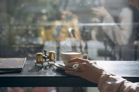 手握着咖啡拿铁热杯的女人在窗外的清晨光线附图片
