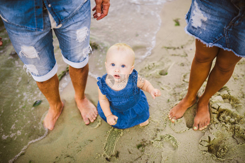 年轻的异恋家庭夫妇白种人妈和爸正在学习在海边的沙滩上牵着孩子的手走路的蹒跚学步的孩子在海滩上的家庭假期图片