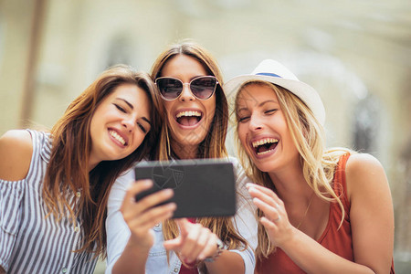 三个快乐笑的女朋友分享平板电脑当她们站在一起近距离看着屏幕时图片