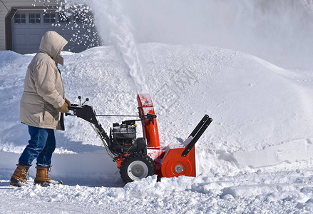 一个不明身份的人利用吹雪机清理冬季暴风雪后的图片