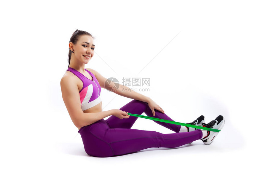 一位身穿型紫色短上衣和健身房的黑发女教练用健身橡皮筋制作和伸展双腿图片