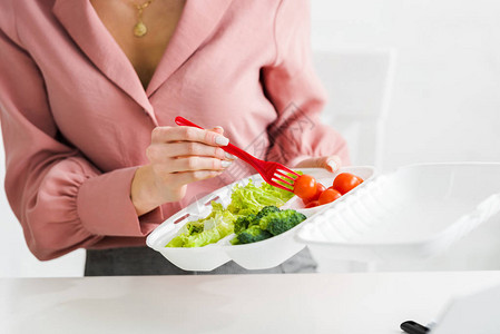 妇女拿着装有机蔬菜和塑料叉子的盒外箱的妇图片