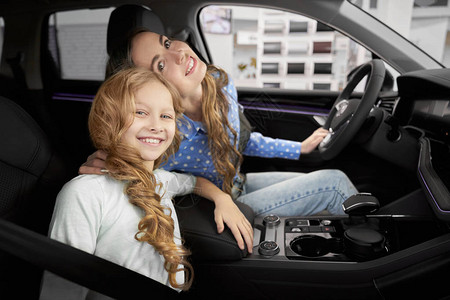 从侧面看漂亮女孩和妈在汽车沙龙坐在新车里图片