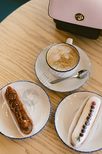 咖啡店里的美味甜法式泡芙和咖啡在一个年轻女孩的光桌上的早餐咖啡手提图片