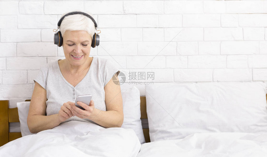 高级女在家床上用智能手机听音乐图片