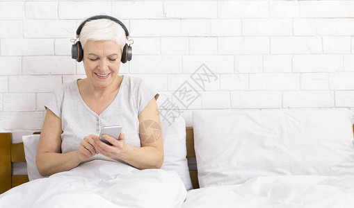 高级女在家床上用智能手机听音乐图片