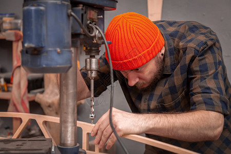 一个穿着工作服戴着木匠帽子的男人正在一个灯光车间的大型钻井机图片