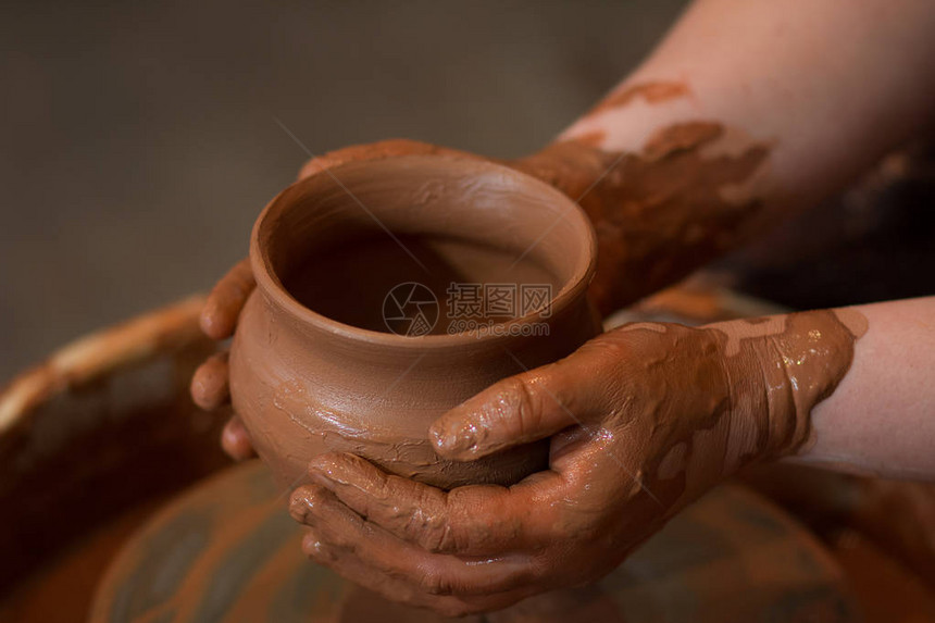 从上面拍摄的旋转陶轮和陶器A用泥杯雕刻双手中的粘土的图片