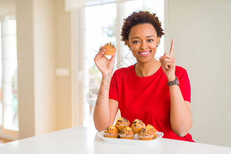 年轻的非洲女吃巧克力薯松饼惊讶于一个想法或问题用快乐的面孔指着手指图片