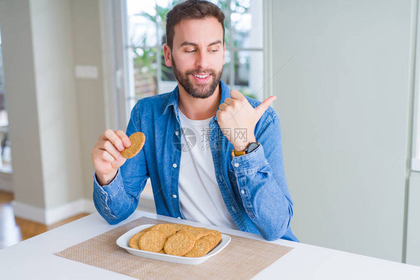 英俊男人吃健康的整个谷物饼干的指尖并用拇指显示在旁边面图片