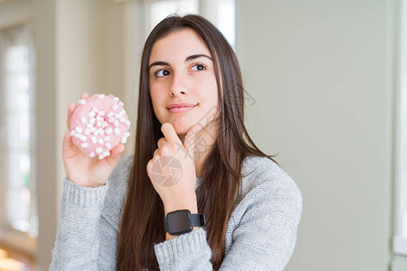 吃糖棉花糖粉甜圈的漂亮年轻女人严肃地思考问题图片