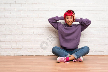 穿着粉色头发坐在地板上的年轻女士感到沮丧图片