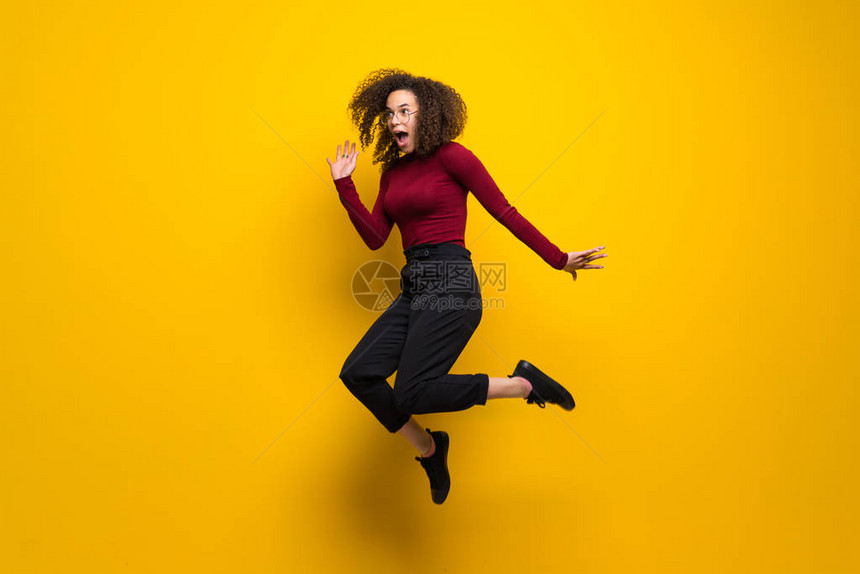 卷发的多米尼加女人跳过孤立的黄色墙壁图片
