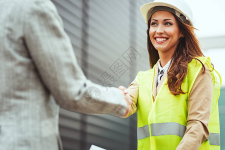 年轻成功的白头盔女工程师与经理握手的图片