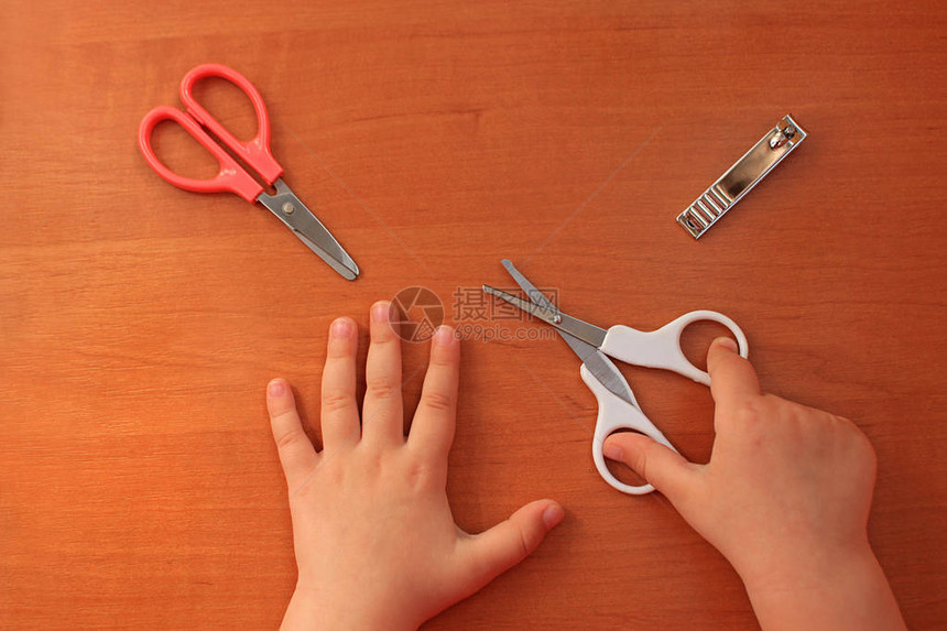 带有圆形尖端和指甲刀的儿童专用剪刀孩子的手和指甲护理儿童美甲木制背景图片