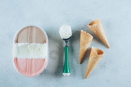 冰淇淋盒带冰淇淋球的勺子和三个华夫蛋筒图片