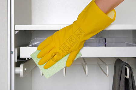 手持橡皮保护手套和微纤维抹布正在房间打扫一个橱柜图片