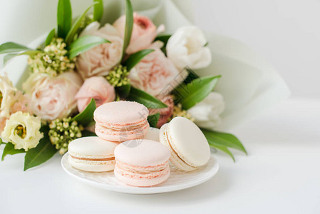 白色桌子特写上优雅的甜马卡龙和柔的米色花朵图片
