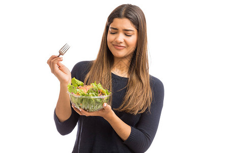 年轻女士对绿色生菜沙拉反感地看着白色背景的图片