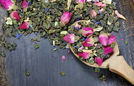 绿茶与鲜花在深色木桌上的木勺绿茶与鲜花和干果片混图片
