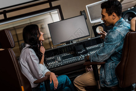 两位年轻的微笑声音制作人在录音室工作时坐在调图片