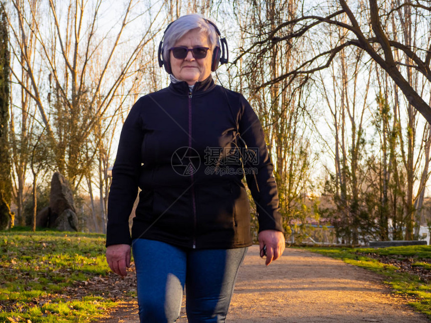 一名白头发的老年妇女在城市公园散步时听音乐图片