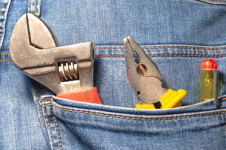 蓝色牛仔裤口袋里的工具钳子和螺背景图片