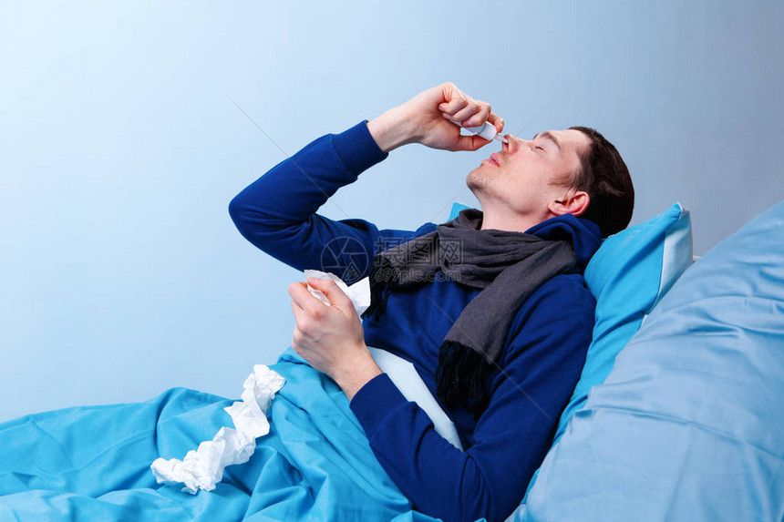 生病的黑褐色男子在躺床上时用鼻喷剂图片