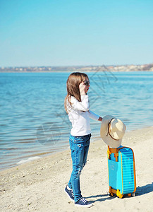 穿着帽子的可爱小女孩在沙滩上拿着手提图片