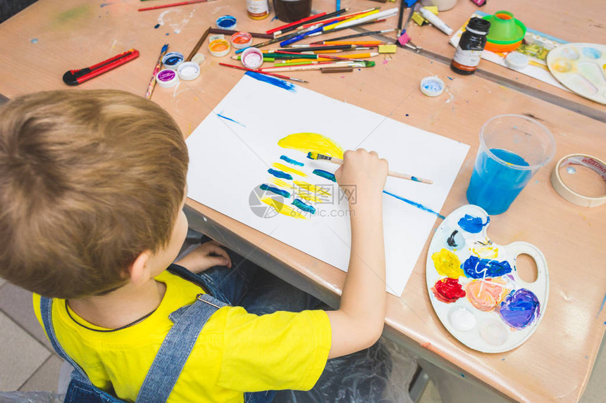 小男孩和一群学龄前学生的老师坐在一起画在maelbert调色板和颜料上绘画回到学图片