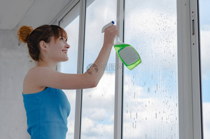 女孩在脏玻璃上喷洒液体以洗窗户图片