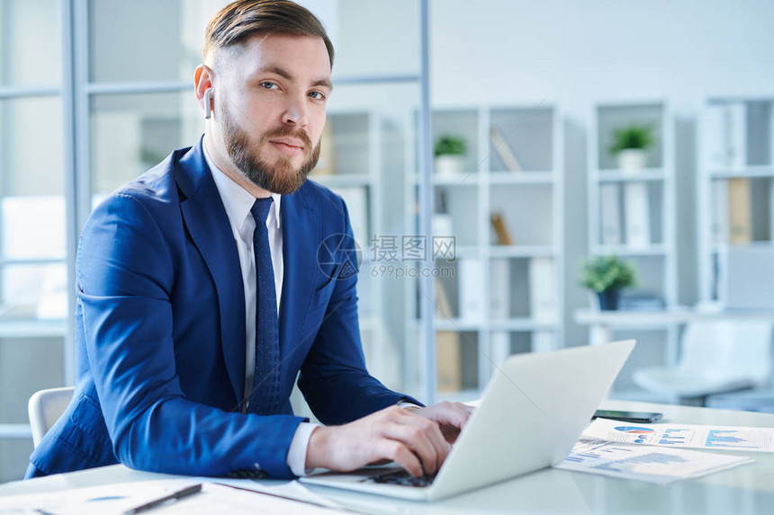 身穿优雅西装和气球的严肃年轻经纪人在坐笔记本电脑前的办图片